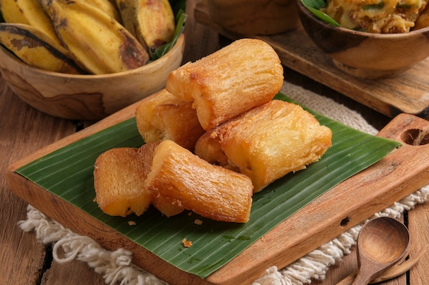 Fried cassava is served on a cutting board with a banana leaf\
base. arranged in such a way with a classic kitchen table\
theme