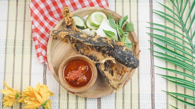 튀긴 메기 또는 신선한 생야채를 곁들인 Pecel Lele은 튀긴 메기, 신선한 야채, 삼발을 곁들인 나무 접시 인도네시아 음식에 제공됩니다.