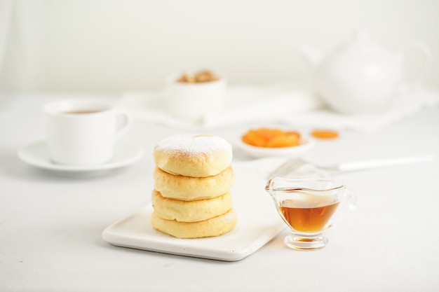 Fried cheese cakes, sweet cheese pancakes on white plate on white background. Home tea party