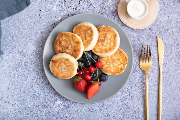 Fried cheesecakes on a plate with sour cream berries and powdered sugar top view