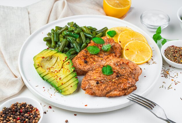 Petto di pollo fritto, avocado, fagioli e limone su sfondo chiaro.