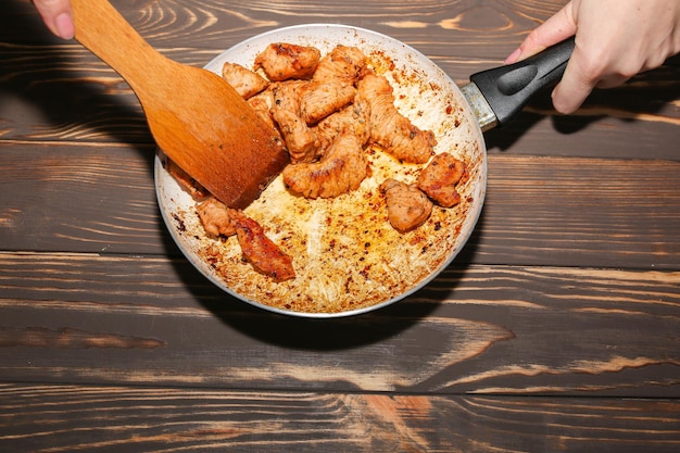 油とスパイスで揚げた鶏の胸肉女性が不健康な食べ物をかき混ぜている焦げた鍋損傷した台所用品木製の背景