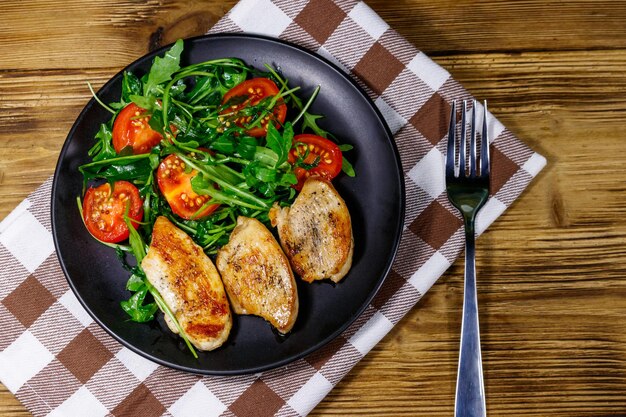 Fried chicken breast with salad of fresh arugula and cherry tomatoes on wooden table Top view