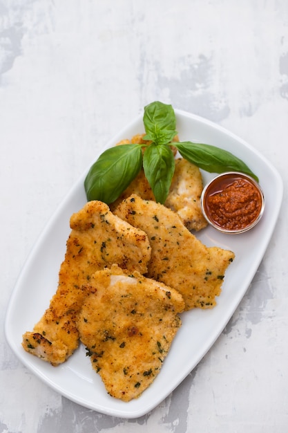 Fried chicken breast with sauce on white dish on ceramic