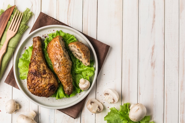 Fried chicken drumstick stuffed with mushrooms flat plate with lettuce leaf on light wood.