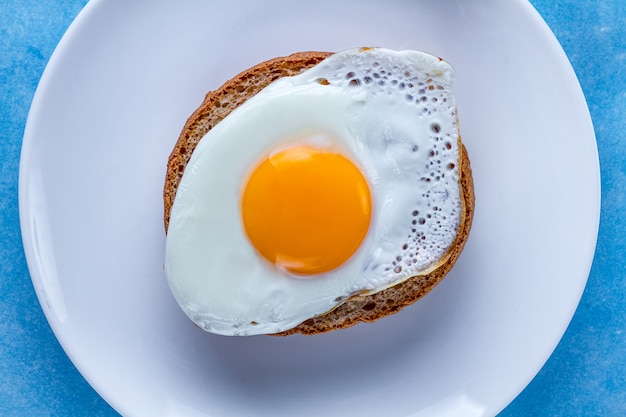 Жареное куриное яйцо с булочкой на тарелку для здорового завтрака. Белковая пища. Вид сверху
