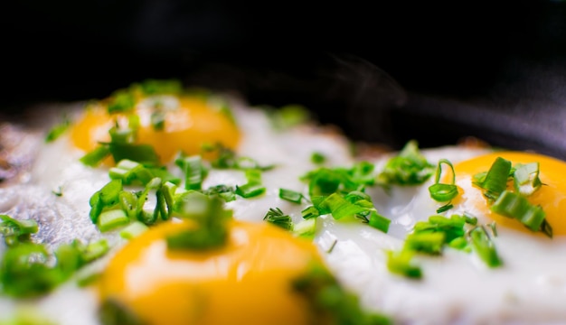 Photo fried chicken eggs with greens and spring onions in a frying pan