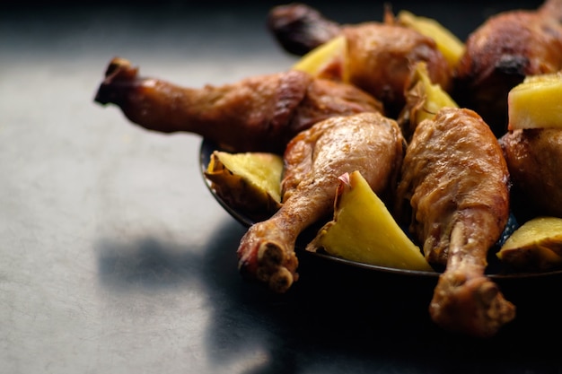 Fried chicken legs with pieces of pineapples on blue plate on black table surface