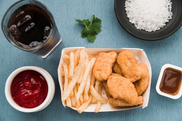 Fried chicken nuggets; french fries; tomato sauce; coriander;\
soft drink on table