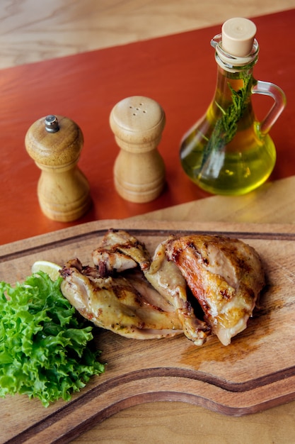 Фото Части жареной курицы на деревянной доске с салатом, помидорами, маслом и специями