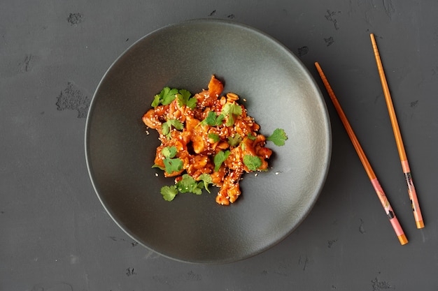 Fried chicken and peanuts with sauce in black ceramic bowl top view, gray background