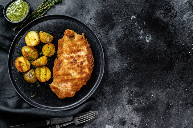 Cotoletta di pollo fritto con patate al forno. superficie nera. vista dall'alto. copia spazio