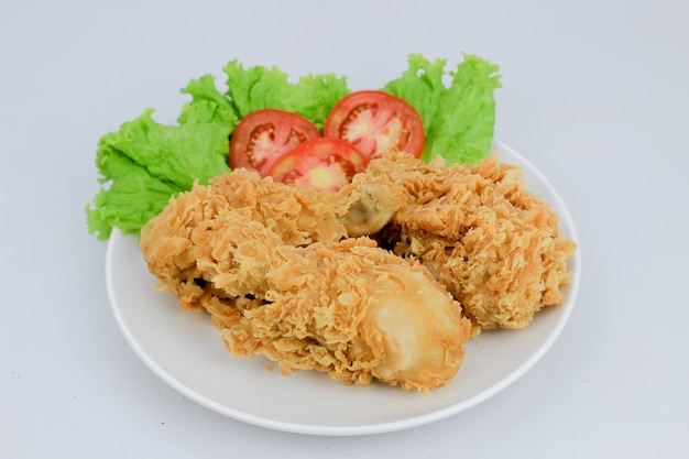 Fried chicken served with lettuce and tomatoes on a plate on a white background