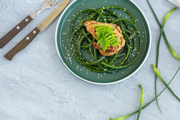 Fried chicken steak with garlic arrows and sesame seeds in green plate on gray concrete table