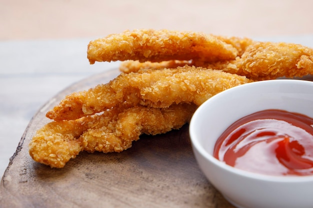 Fried chicken strips with tomato sauce on wooden table