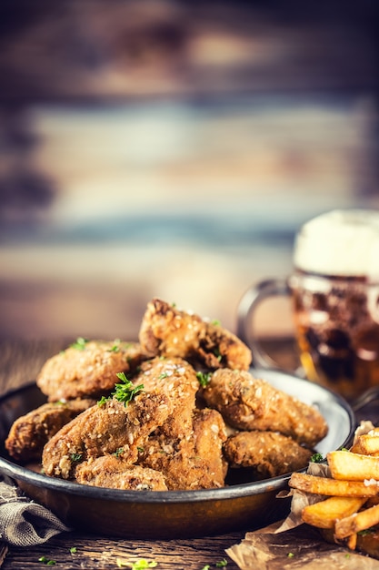 Fried chicken wings fries and draft beer on table in pub or restaurant.