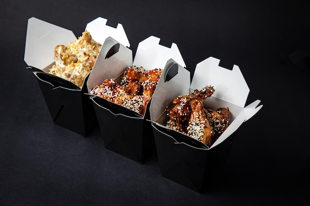 fried chicken wings with sauce and cheese in a delivery box on a black background