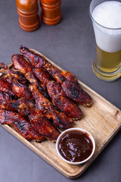 Fried chicken wings on a wooden board with barbecue sauce and a glass of beer.