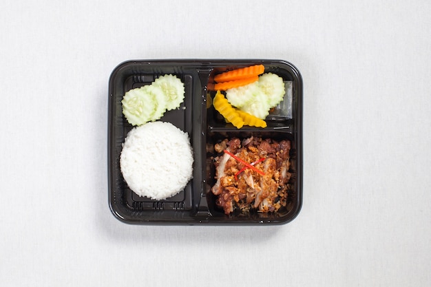 Photo fried chicken with garlic and pepper and rice put in black plastic box, put on a white tablecloth, food box, thai food.