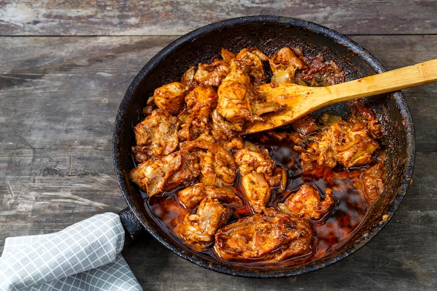 Жареная курица со специями на сковороде с деревянной лопаточкой на темном столе