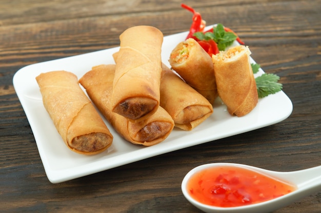 Photo fried chinese spring rolls served with chili sauce and decorated rose tomatoes with green leaved on wood, space. concept asian food