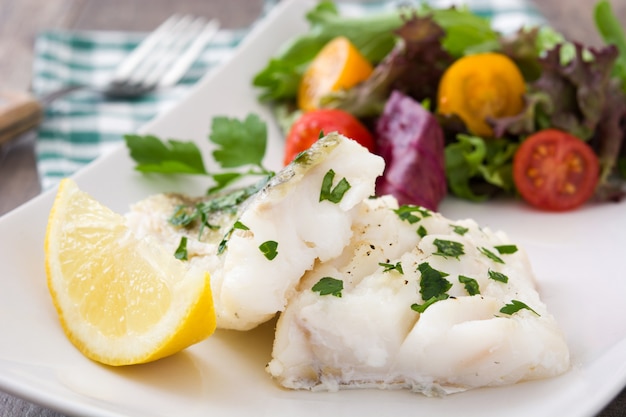 Fried cod fillet and salad on wooden table  close up