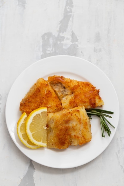 Fried cod fish with lemon on white plate