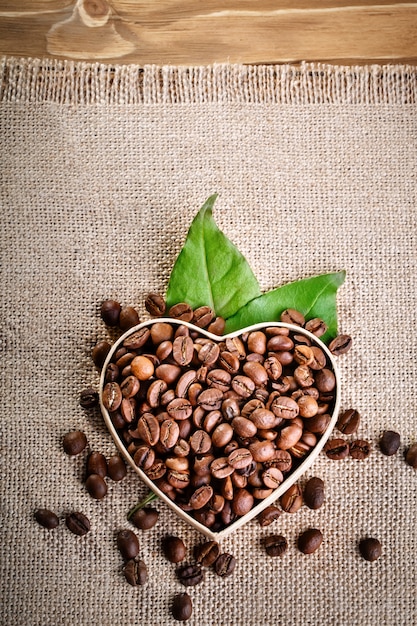 Fried coffee beans lie in the form of heart on wooden boards and burlap.