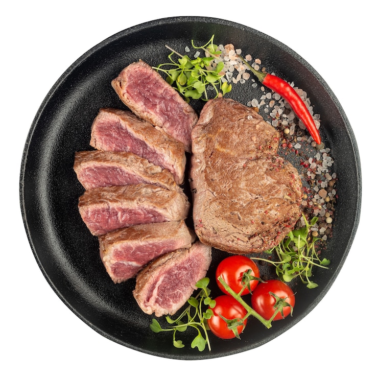 白地に隔離された鋳鉄製の鍋で、新鮮な野菜、トマト、ハーブ、スパイスを細かく切ったビーフステーキの炒め物。上面図。