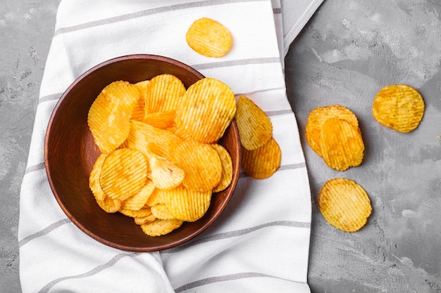Photo fried corrugated golden potato chips in brown wooden bowl on tablecloth towel