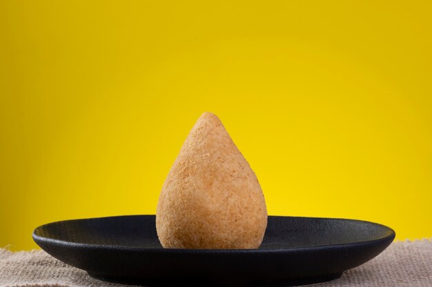 Fried coxinha on black plate with yellow background.