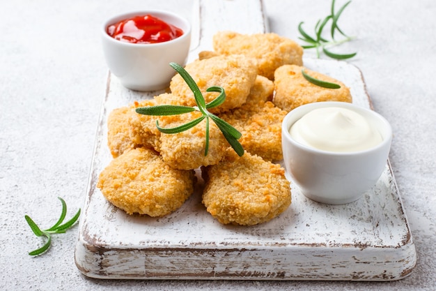 Fried crispy chicken nuggets with popular sauces on gray background