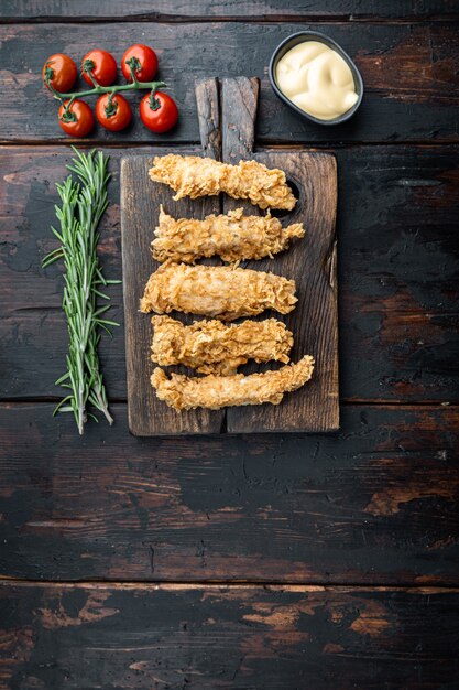 Fried crispy chicken stripes parts on old dark wooden table, top view.