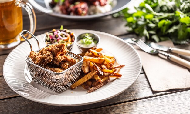 Fried crispy chicken wings with chips, dip and salad served on a table.