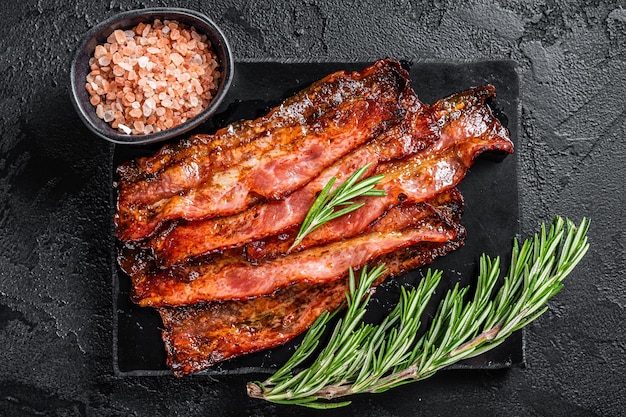 Photo fried crunchy streaky bacon stripes black background top view