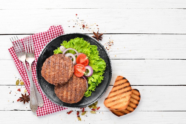 Fried cutlet for burger with vegetables In a black plate on a wooden background Top view Free space for your text Flat lay