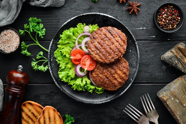 Fried cutlet for burger with vegetables In a black plate on a wooden background Top view Free space for your text Flat lay