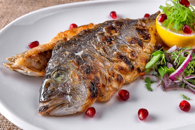 Fried Dorado fish with lemon and herbs on a plate