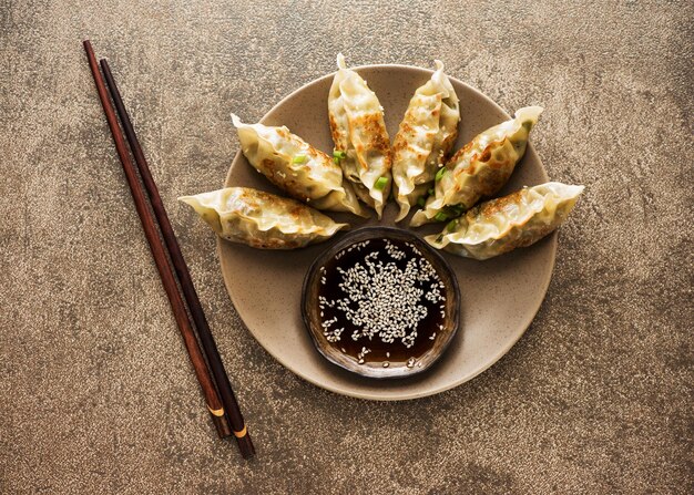 Жареные пельмени Gyoza на тарелке соевого соуса и палочки для еды на каменном фоне вид сверху