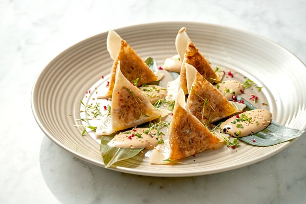 Fried dumplings or Japanese Gyoza in yellow sauce, cherry tomatoes and green peas, served in a white plate on a marble table. Pan-Asian cuisine. Restaurant food