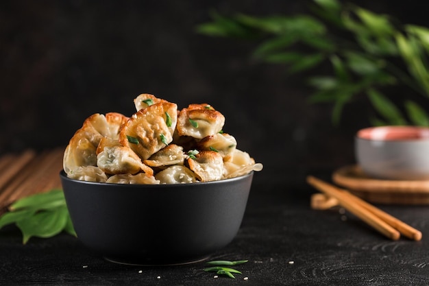 Gnocchi fritti con carne di maiale ed erbe aromatiche in una ciotola rotonda nera su sfondo scuro con le bacchette cibo coreano vista laterale con copypaste per testo orientamento orizzontale