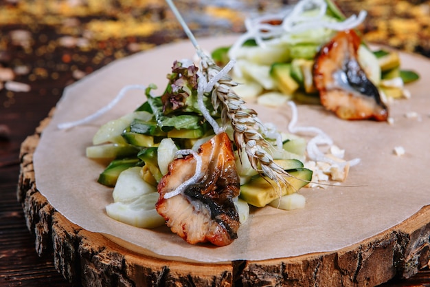 Fried eel with freshly cut vegetables. Dish on a wooden stand