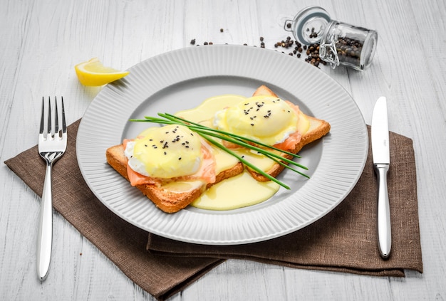 Uovo fritto su pane per la colazione sul piatto e sulla tavola rustica con i salmoni