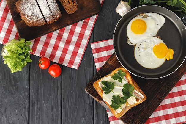 Жареное яйцо в сковороде с нарезанным хлебом на деревянном столе