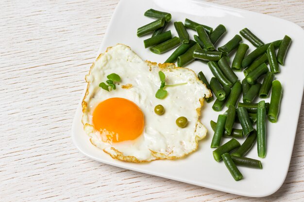 흰 접시에 튀긴 계란과 녹색 콩입니다.