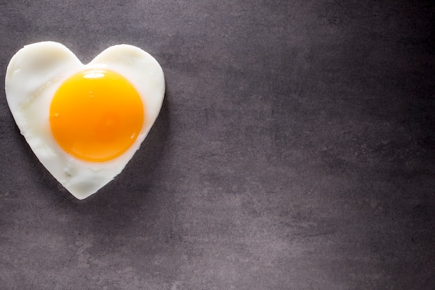 Fried egg heart-shaped and gray background.