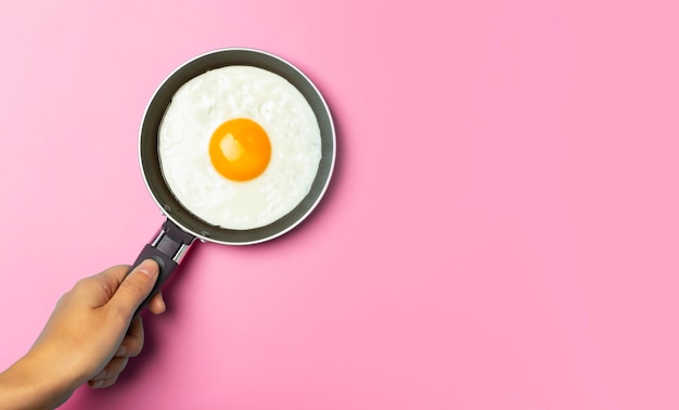 Fried egg is minimal fried egg in a frying pan on an empty pink\
background creative breakfast