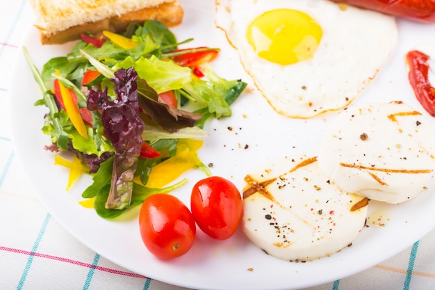 Fried egg and sausage on the plate with green salad and cheese