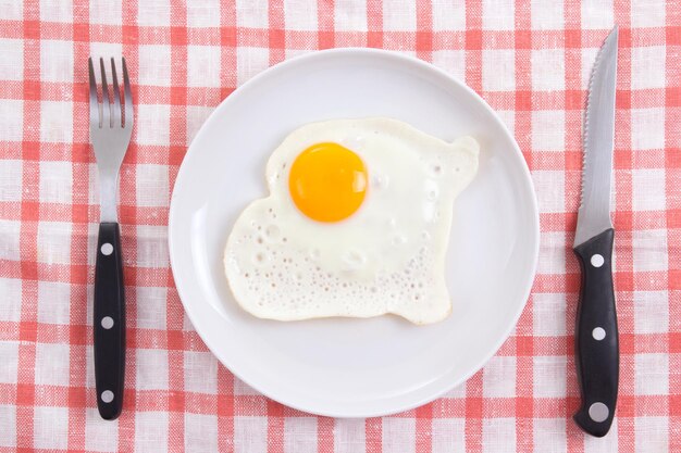 Fried egg in white plate with fork and knife on the table