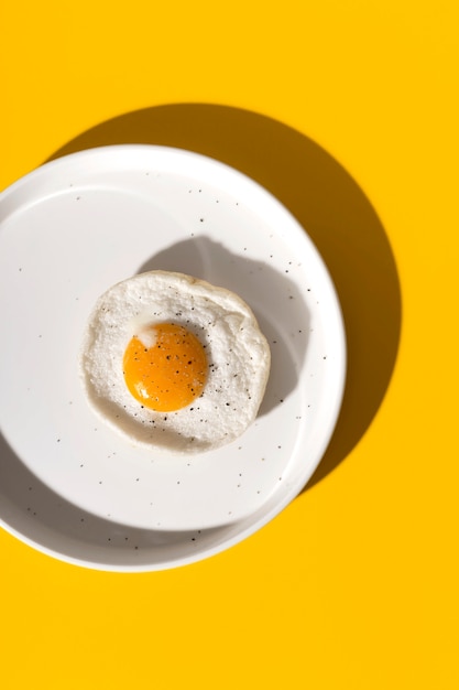 Fried egg on white plate on yellow with shadows.